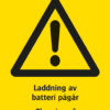Varningsskylt med symbol för varning för fara och texten "Laddning av batteri pågår" samt på engelska "Charging of battery in progress".